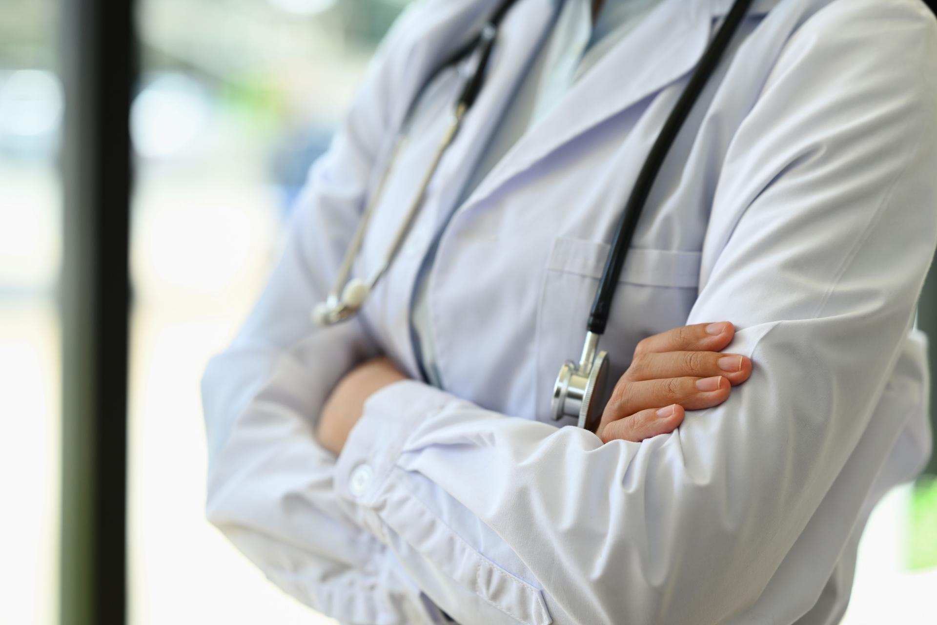 Unrecognizable general practitioner standing with arms crossed standing near window in hospital